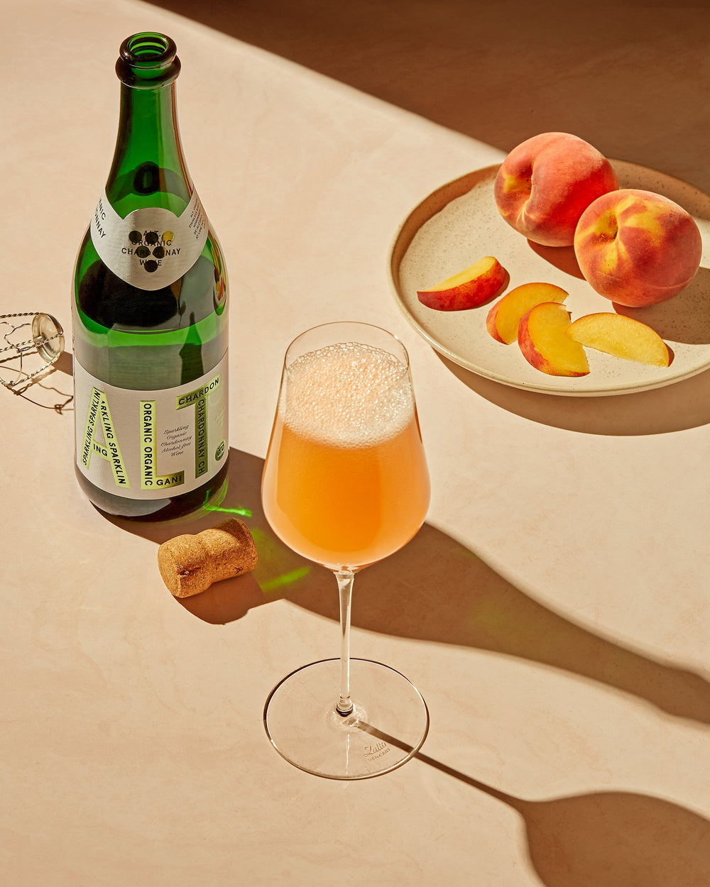 Bilde av ALT. Blanc de Blancs og et vinglass bestående av den og ferskenjuice. Et fat ved siden av med ferskenbiter på.